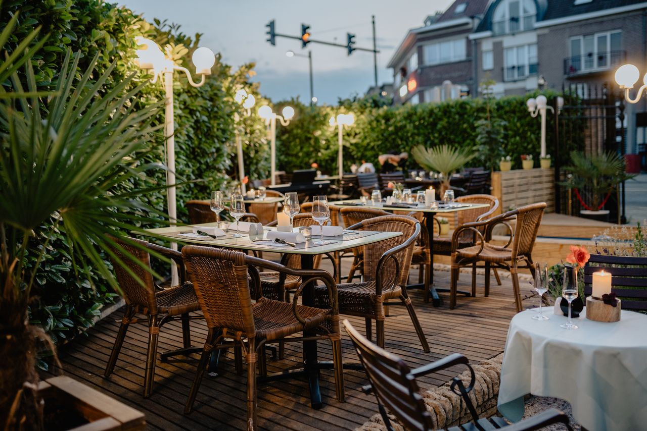 Terraza de restaurante con sillas de mimbre y luces encendidas.