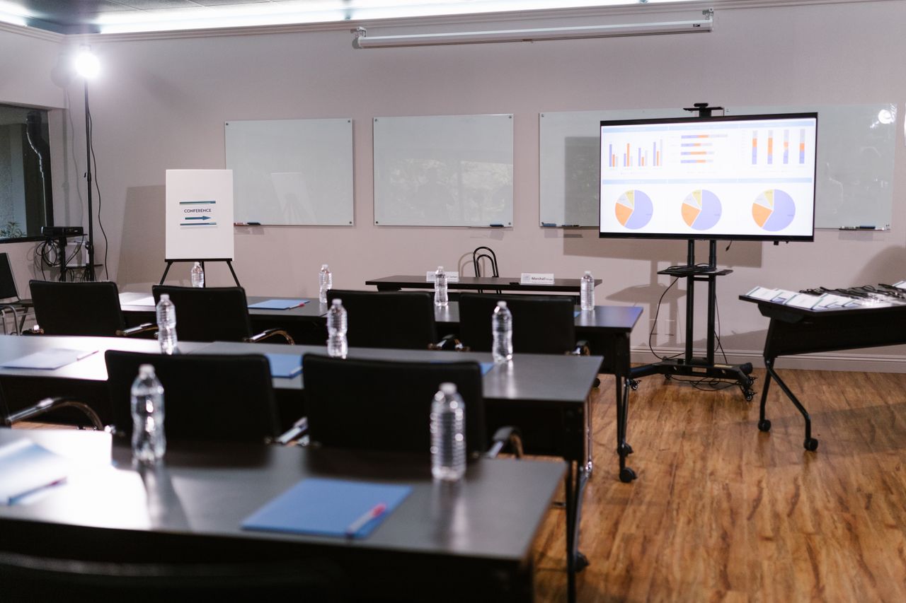 Aula con mesas, sillas y una pantalla para presentaciones.